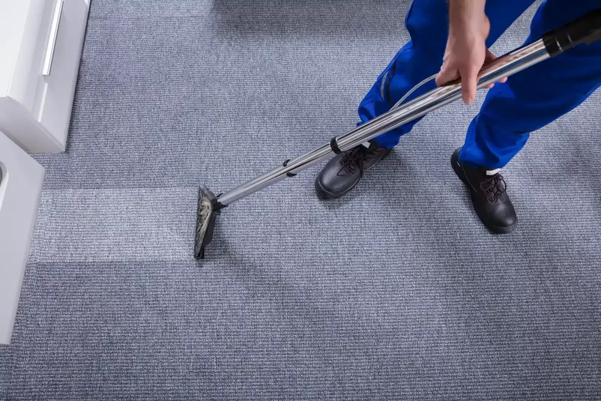 A person in blue uniform cleans a carpet with a professional cleaning machine.
