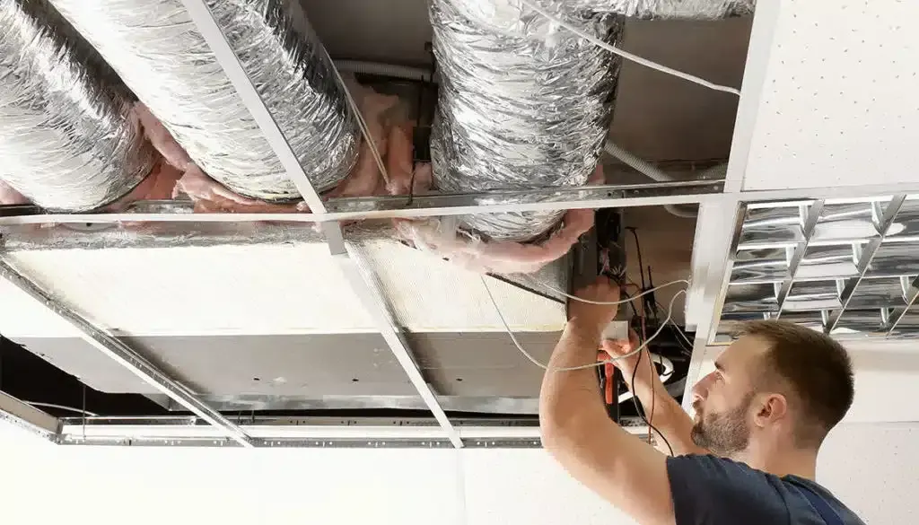 Technician working on air ducts in a commercial ceiling.