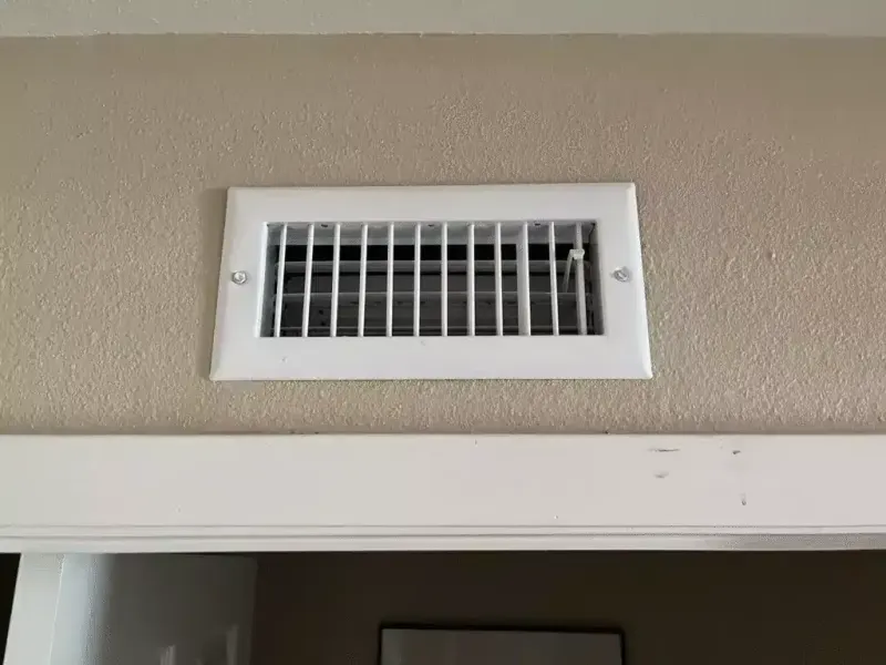 Close-up of a white air vent on a textured wall.