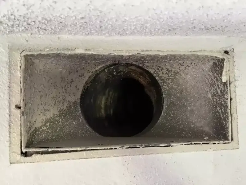 Close-up of a dirty air duct vent with visible dust and grime inside the opening.