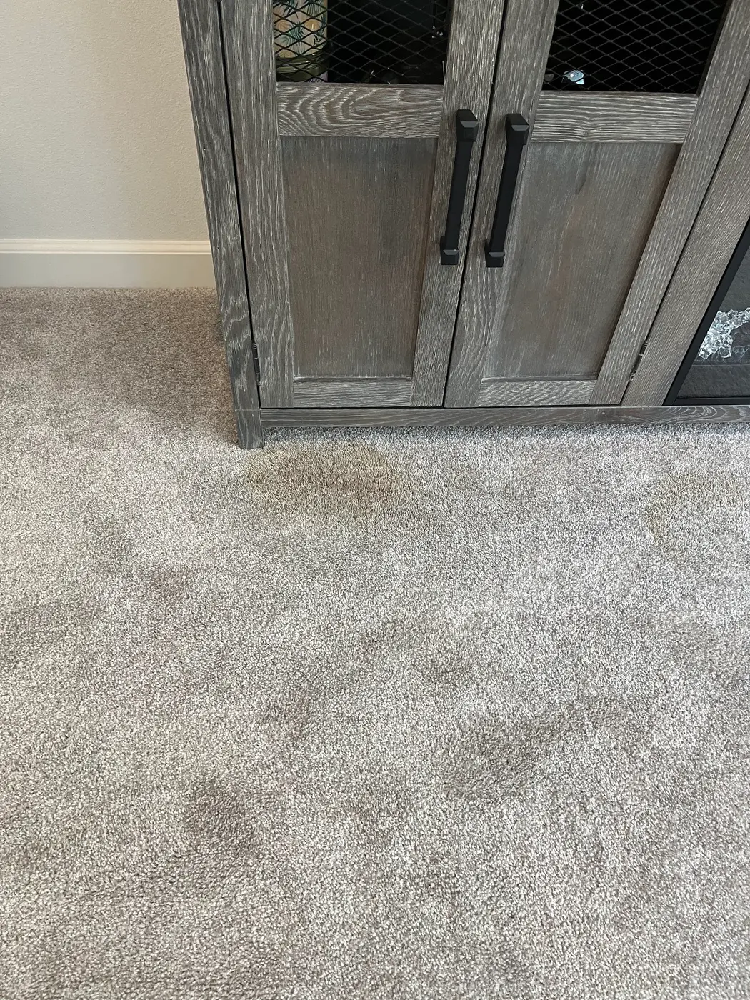 Carpet spot by a cabinet beside the cleaned carpet before cleaning