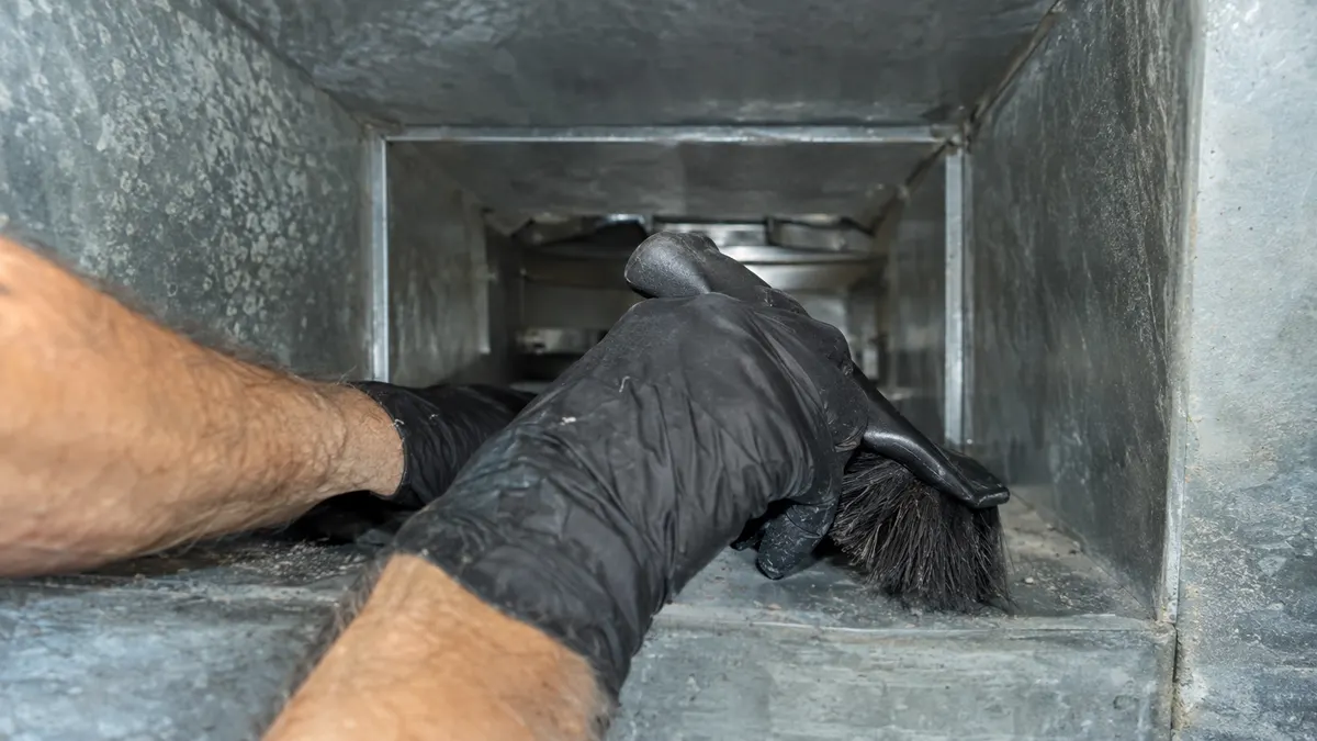 Technician cleaning a supply register with a HEPA vacuum hose
