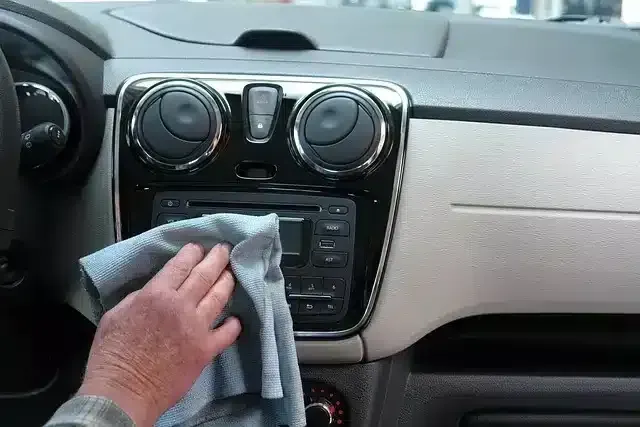 A hand wipes down the dashboard of a car with a microfiber cloth.