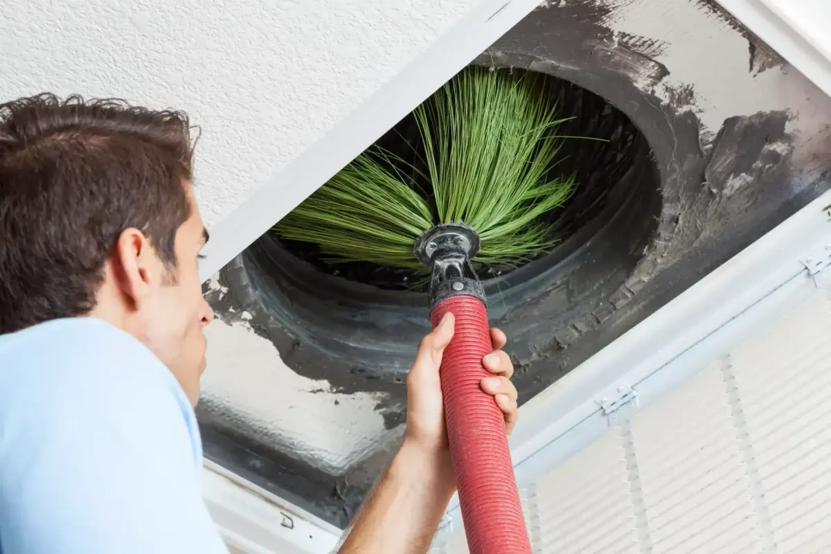 Technician cleaning an air duct with a brush attachment on a hose.