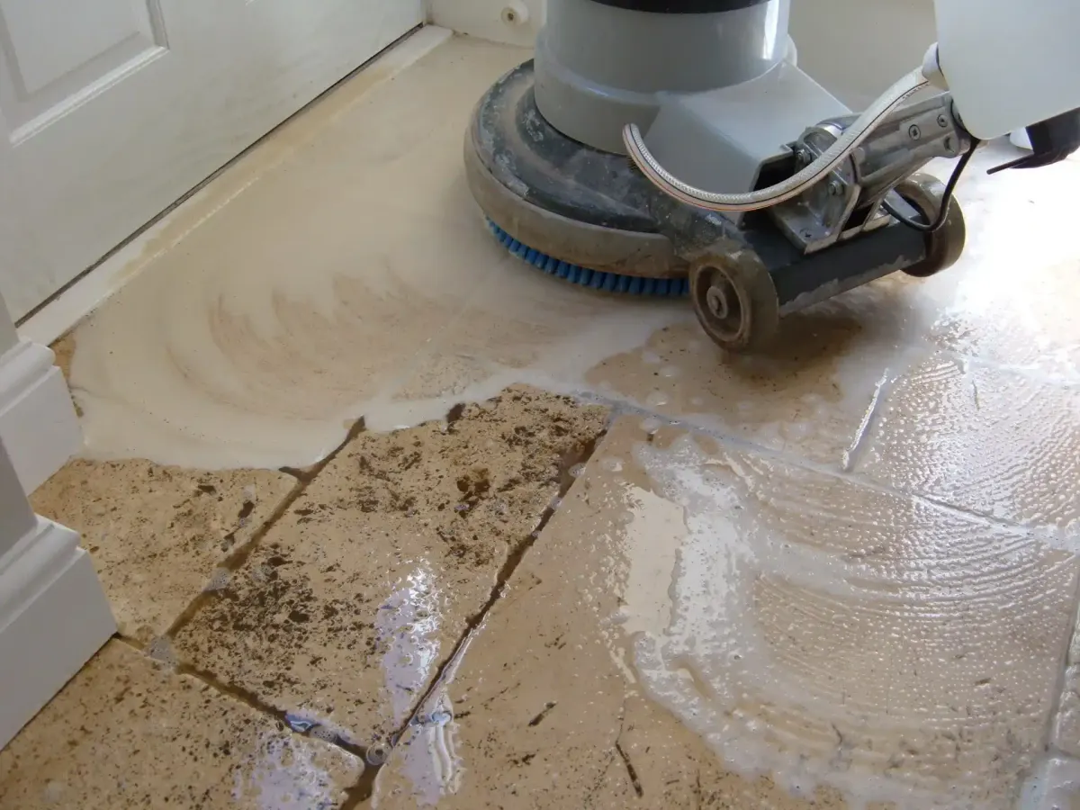 A floor cleaning machine scrubs a dirty tile floor with soap and water.