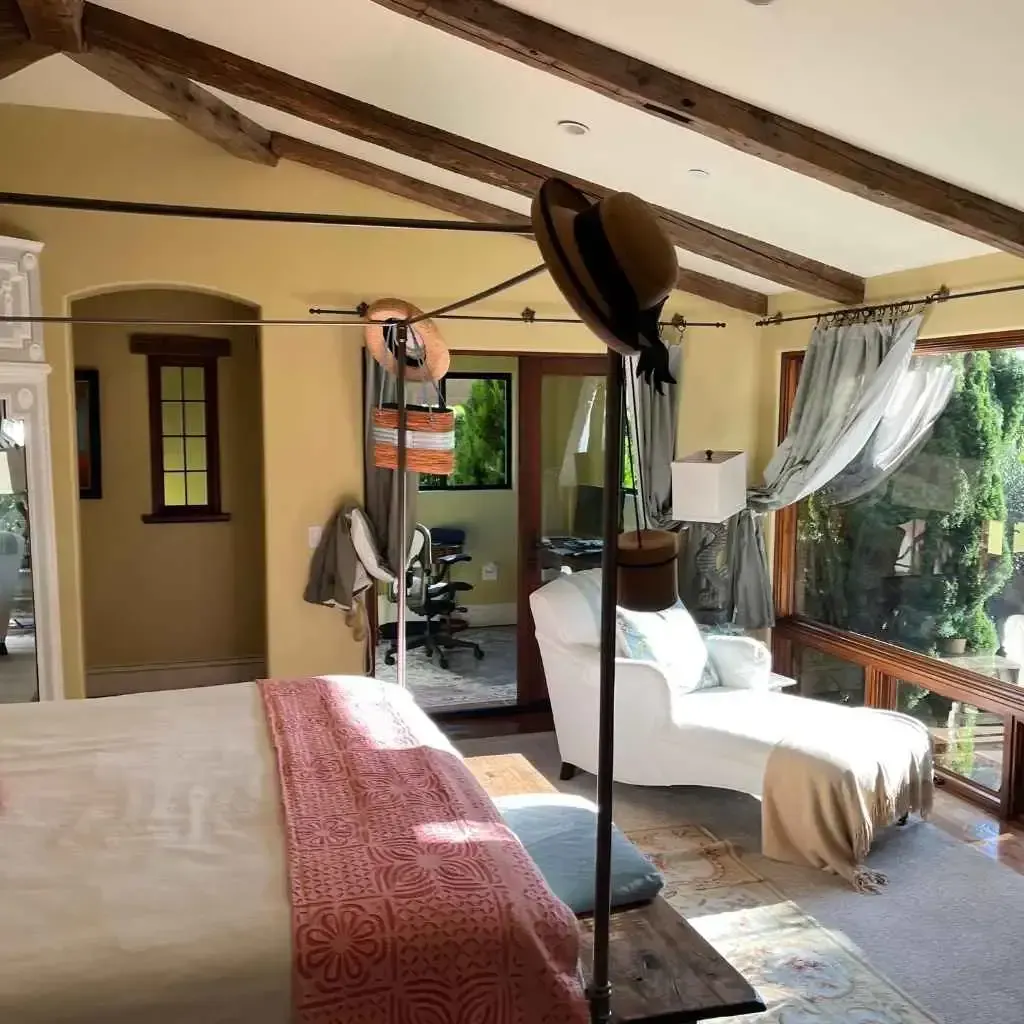 Bedroom with a bed, chaise lounge, and large windows overlooking greenery.