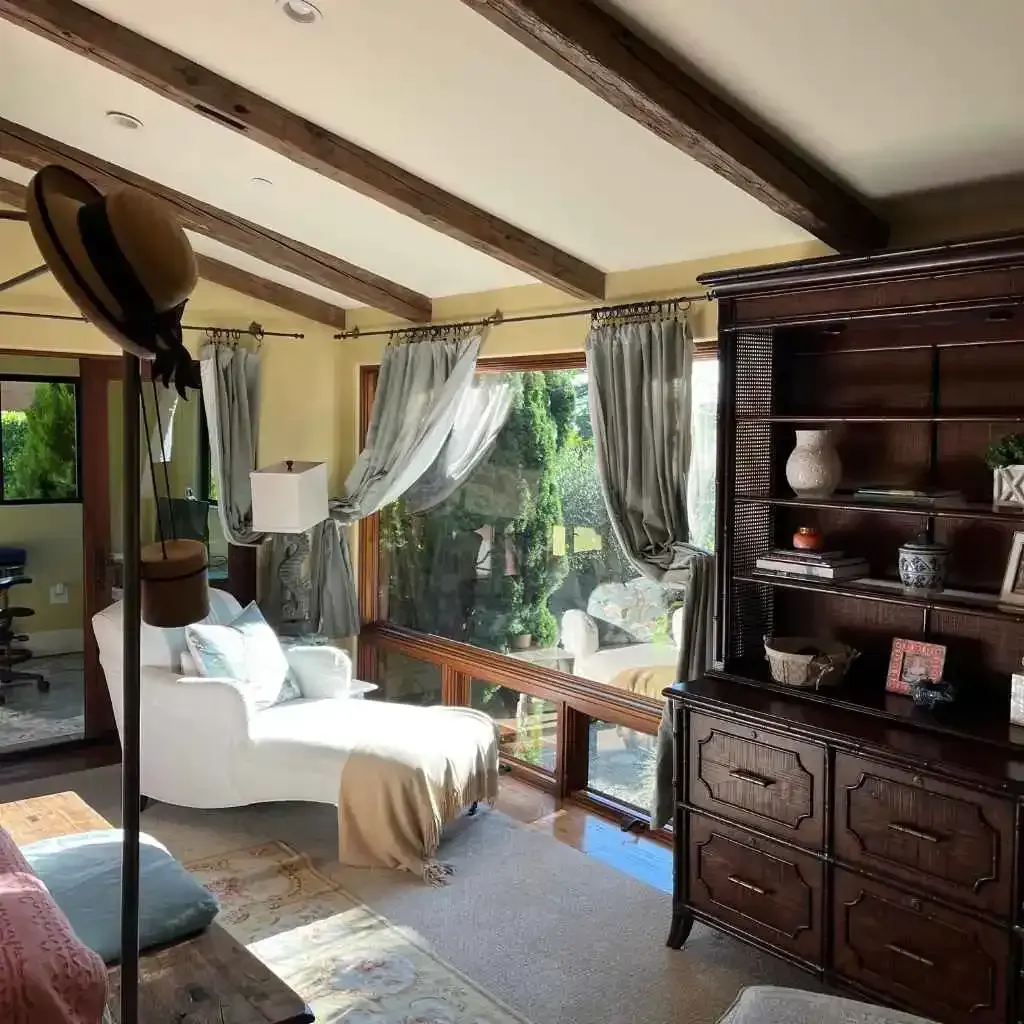 Sunlit living room with a chaise lounge, large windows, and a bookshelf.