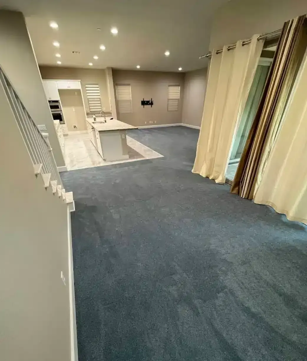 A clean, blue carpet covers the floor of a modern living room with a kitchen island.
