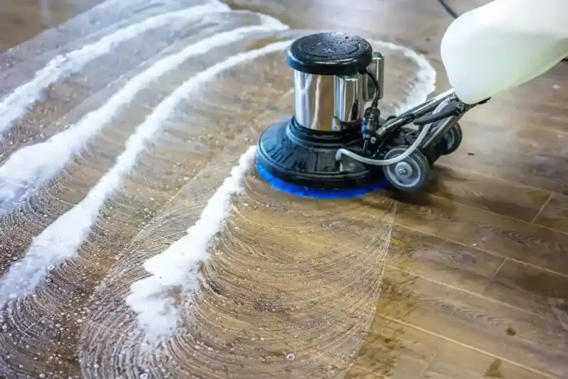 A floor cleaning machine scrubs a wooden floor with soap and water.