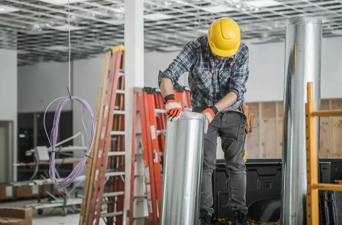 Construction worker installing metal ductwork in a building under renovation.