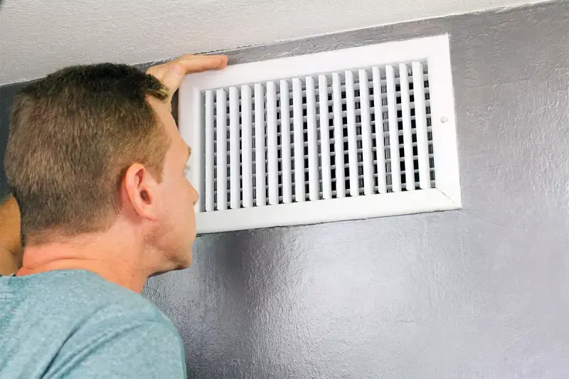 Man inspecting an air vent on a silver wall