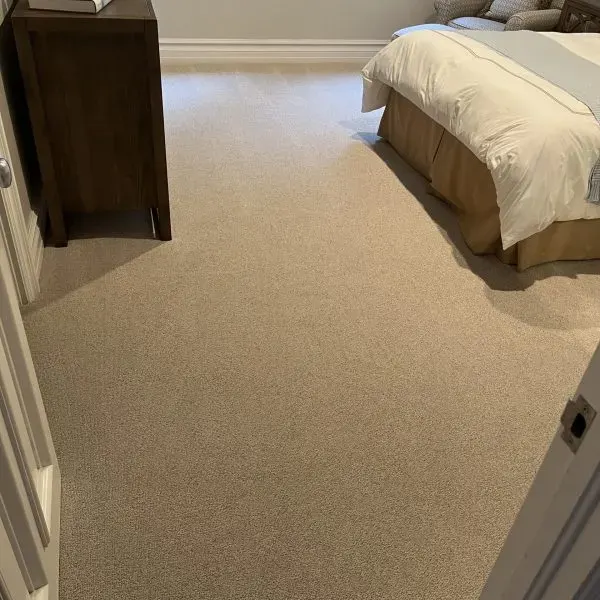 Clean, neutral-colored carpet in a bedroom with a dresser and bed.
