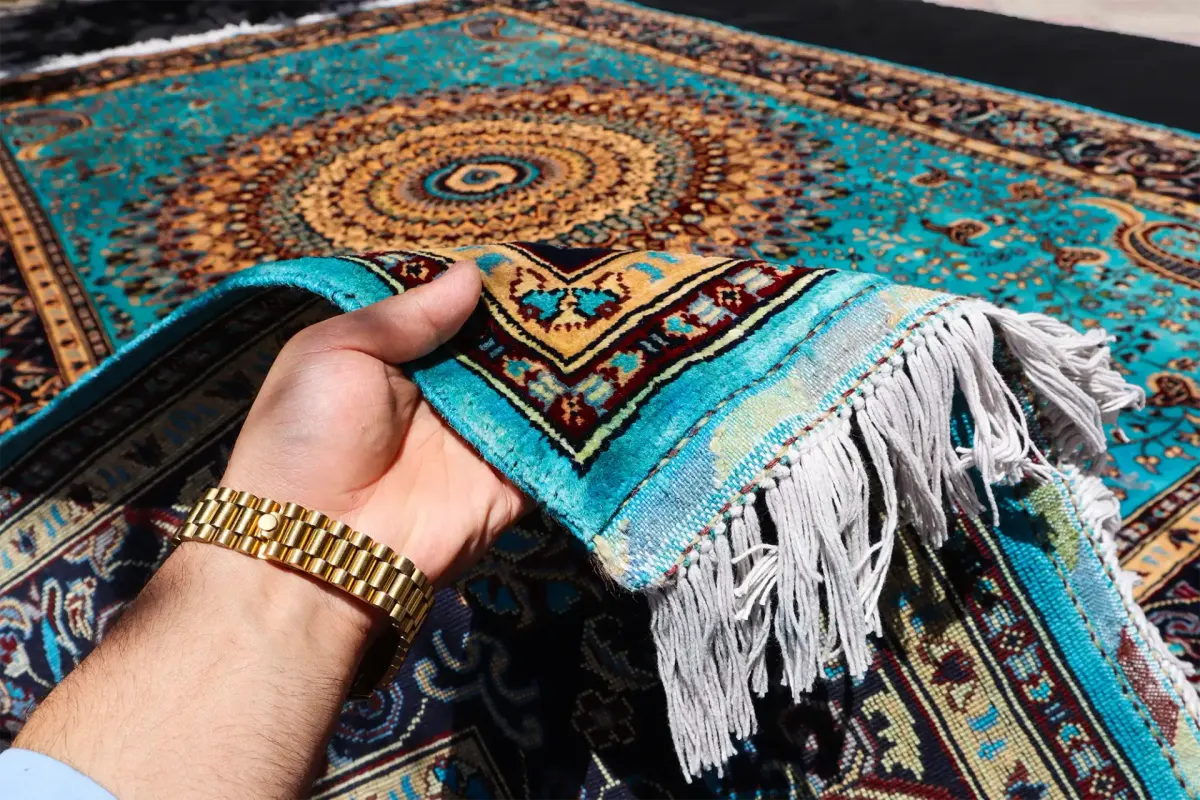 Close-up of a hand holding a corner of a vibrant oriental rug with intricate patterns.
