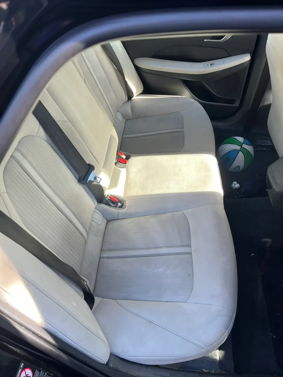 Interior view of a car's back seat, showing clean upholstery and a basketball on the floor.