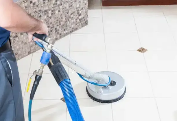 A person cleaning white tile floors with a rotary cleaning machine.