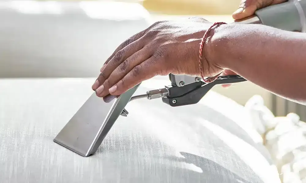 Close-up of a hand using a cleaning tool on a white couch cushion.