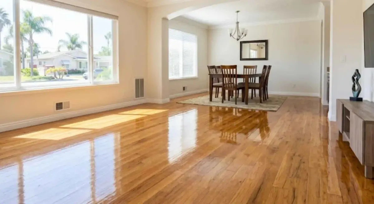 Shiny hardwood floors in a sunlit dining and living area with palm trees visible outside.