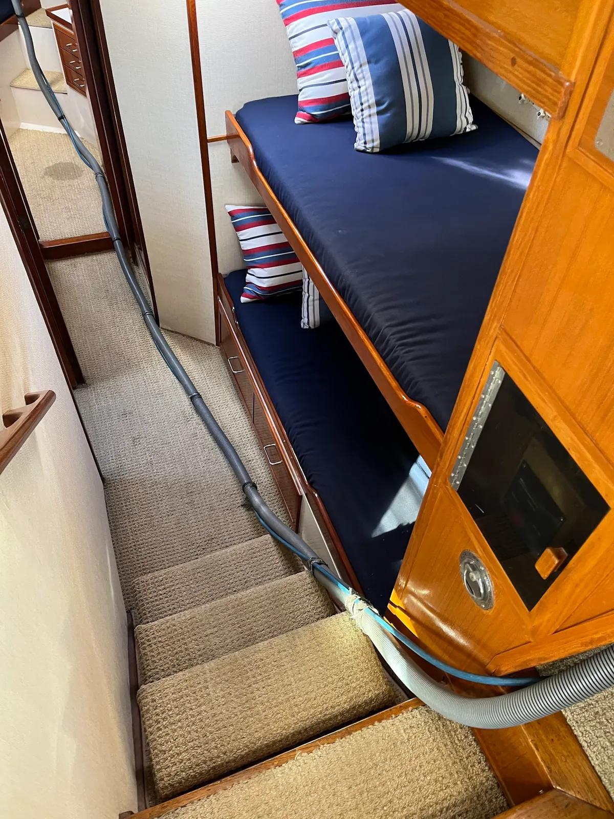 Cleaning hose run down the carpeted stairs of a boat cabin with bunks