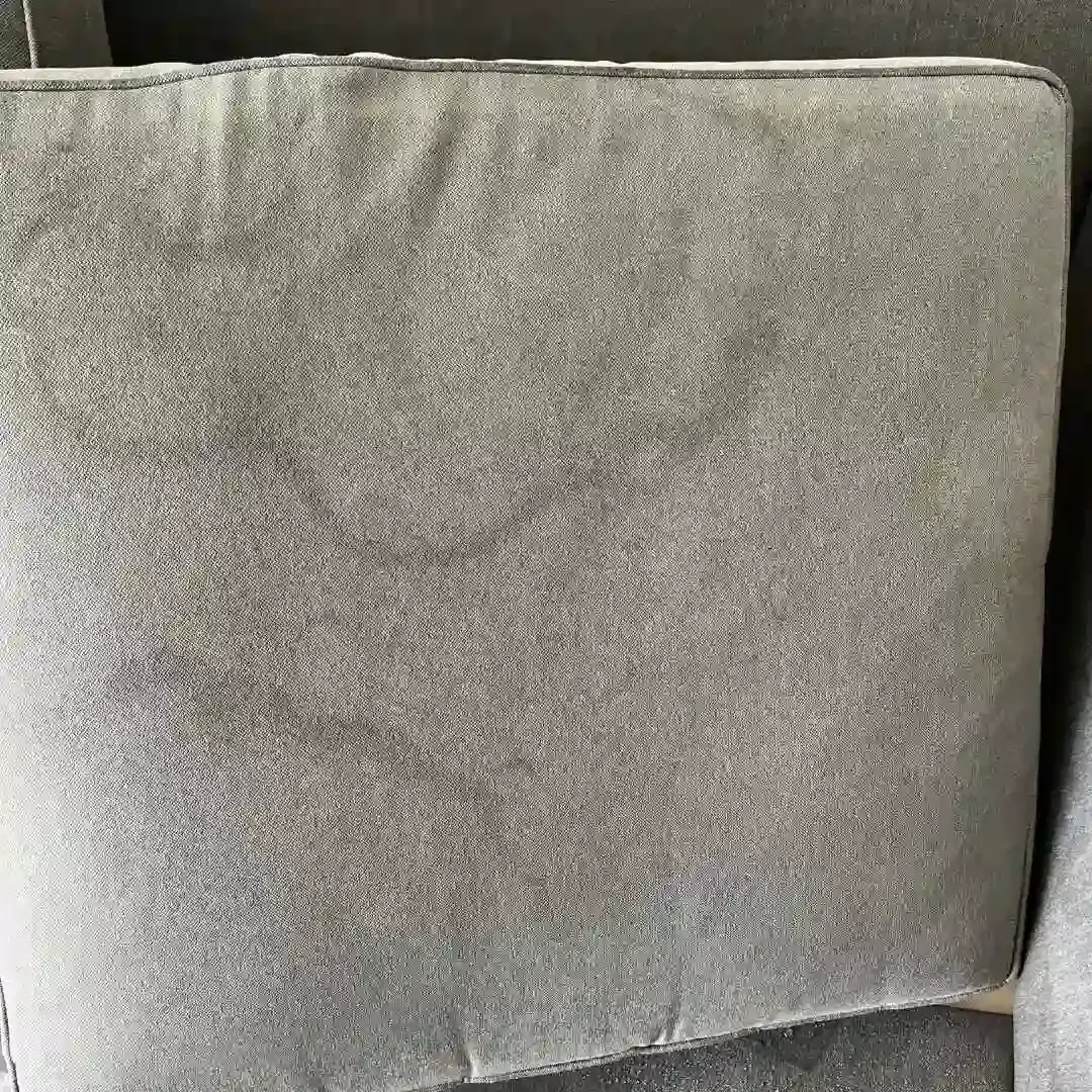 Close-up of a stained gray couch cushion showing dark marks and discoloration.