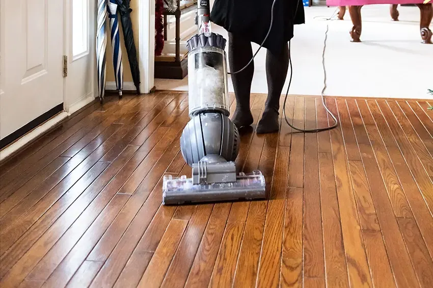 Person vacuuming a shiny hardwood floor with a Dyson vacuum cleaner.